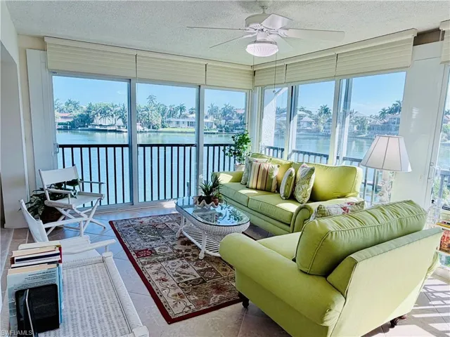 Expansive windows with horizontal blinds, ceiling fan with integrated lighting, tiled flooring, and a black metal balcony railing