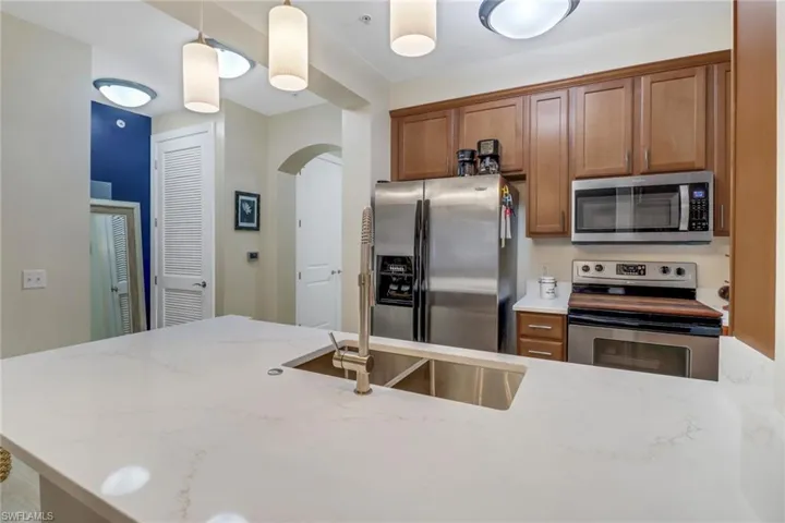 Kitchen with stainless steel appliances, light stone counters, and pendant lighting