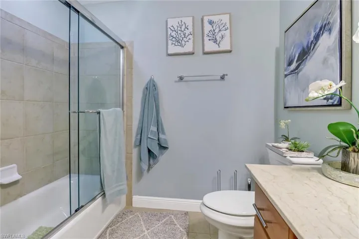 Full bathroom with bath / shower combo with glass door, vanity, tile patterned floors, and toilet