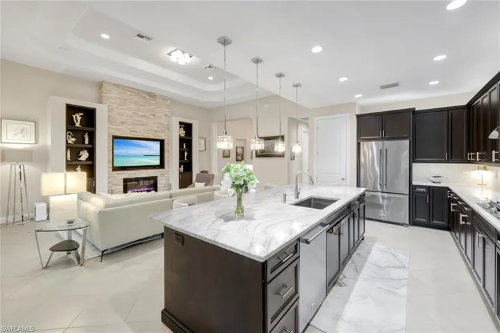 Kitchen featuring decorative light fixtures, a large fireplace, light stone countertops, stainless steel appliances, and open floor plan