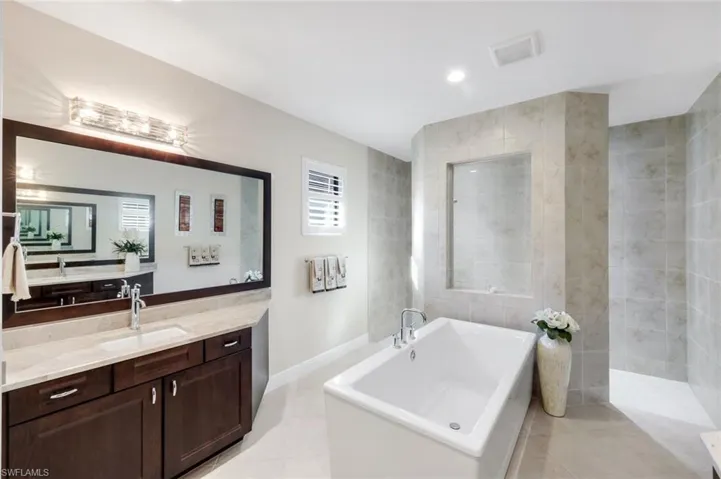 Bathroom with tile walls, vanity, a freestanding tub, light tile patterned flooring, and recessed lighting