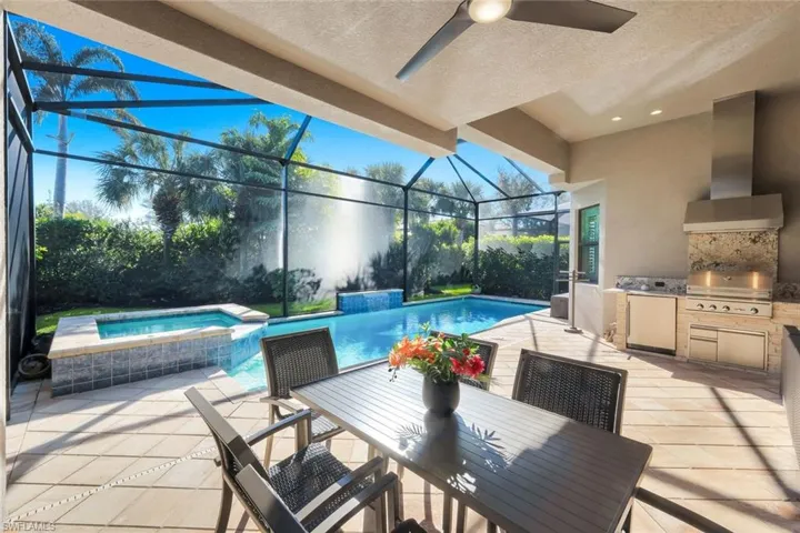 Relaxing pool / spa with a sunroom, a patio, an outdoor kitchen / dining area, and glass enclosure