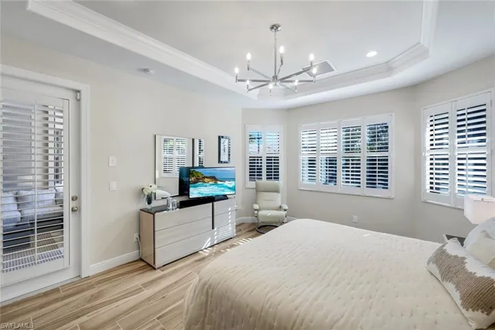 Bedroom featuring suspended lighting, wood tiled floors, a tray ceiling, ornamental molding, and access to outside
