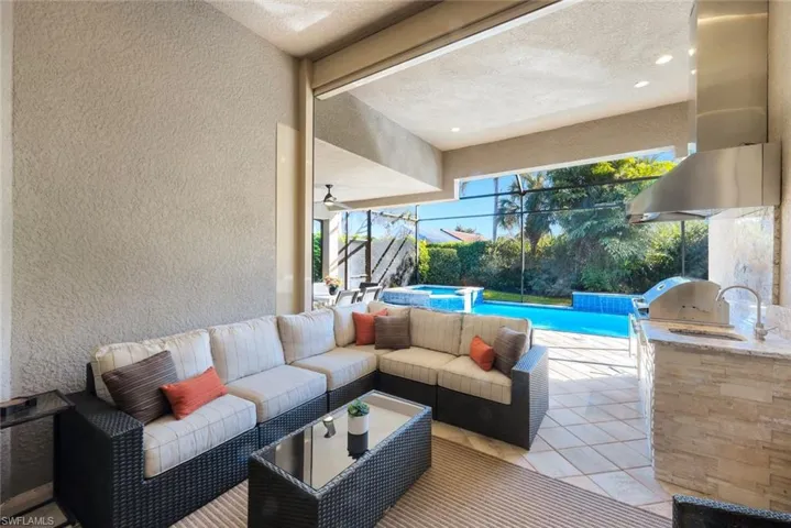 View of patio featuring an outdoor kitchen and area to lounge, a pool with connected hot tub, and glass enclosure
