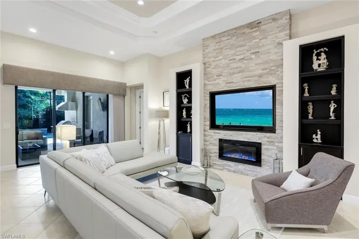 Living room featuring built in features, a stone fireplace, recessed lighting, light tile patterned floors, and ornamental molding