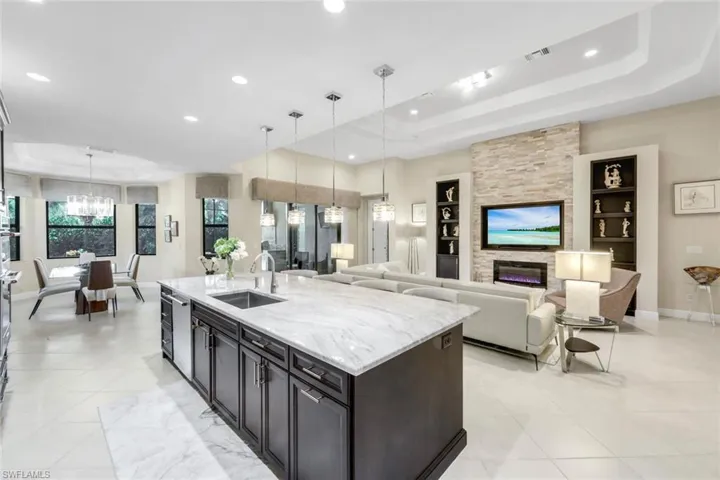 Kitchen with a raised ceiling, light stone countertops, a kitchen island with sink, a fireplace, and open floor plan