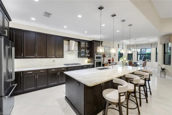 Kitchen featuring light stone countertops, stainless steel appliances, backsplash, a kitchen breakfast bar, and a large island with sink