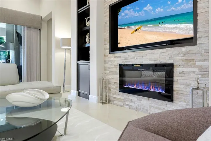 Living room with built in features, a stone fireplace, and tile patterned flooring