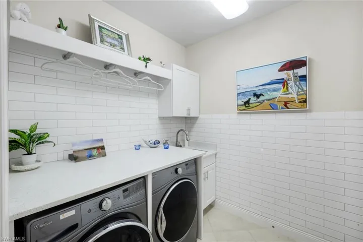 Laundry room with tile walls, separate washer and dryer, a wainscoted wall, cabinet space, and light tile patterned floors