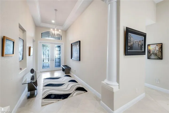 Foyer featuring decorative columns, french doors, light tile patterned flooring, suspended lighting, and a high tray ceiling