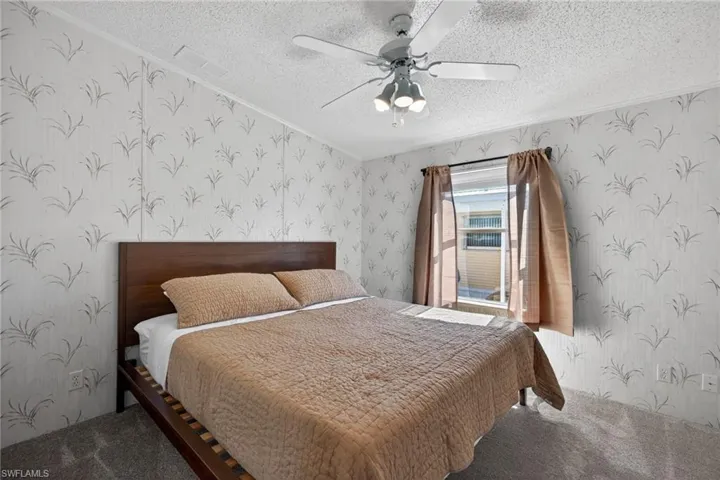 Carpeted bedroom with wallpapered walls, a textured ceiling, and ceiling fan