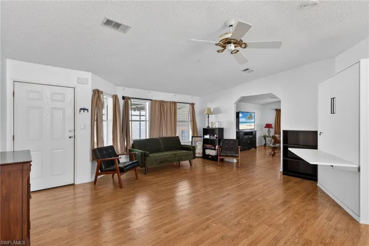 Living area featuring arched walkways, light wood-style floors, a textured ceiling, and ceiling fan