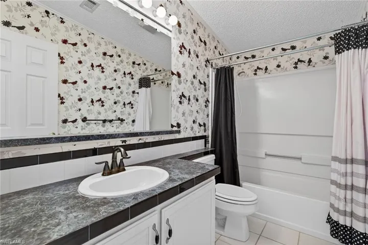 Full bath featuring shower / bathtub combination with curtain, vanity, a textured ceiling, light tile patterned floors, and wallpapered walls