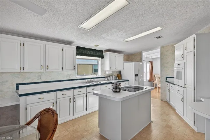 Kitchen with wallpapered walls, a center island, a textured ceiling, white cabinetry, and white appliances
