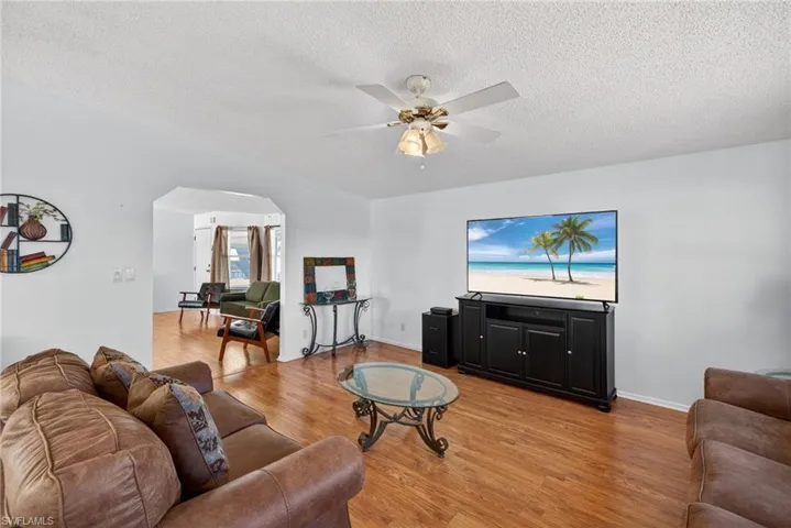 Family room featuring light wood-type flooring, arched walkways, a textured ceiling, and a ceiling fan