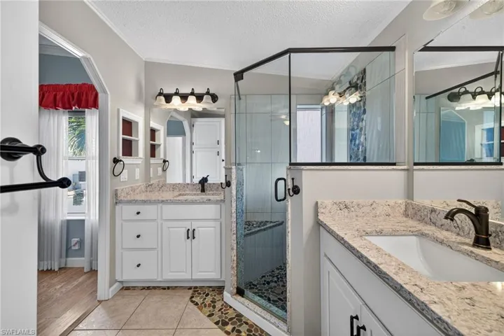 Primary Bathroom featuring a stall shower, two vanities, light tile patterned floors, a textured ceiling, and crown molding