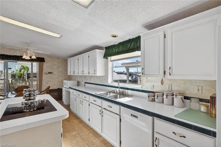Kitchen with white cabinets, white appliances, a ceiling fan, tile countertops, and wallpapered walls