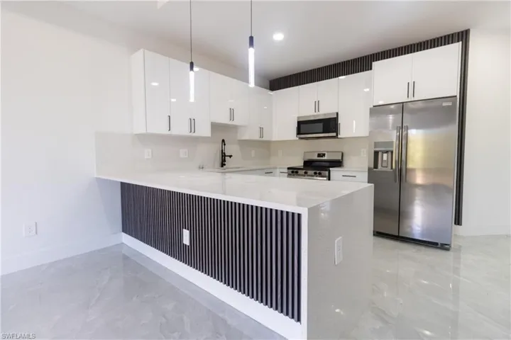 Kitchen with stainless steel appliances, white cabinets, a peninsula, and light stone counters