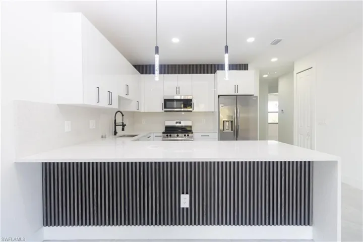 Kitchen featuring a peninsula, stainless steel appliances, light stone countertops, and white cabinetry