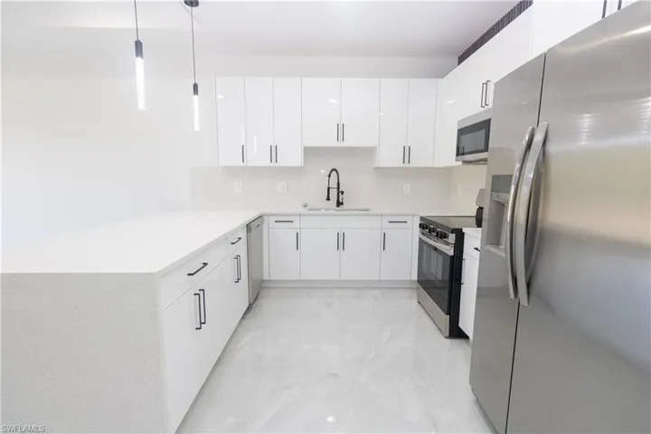 Kitchen with stainless steel appliances, a peninsula, hanging light fixtures, and white cabinets