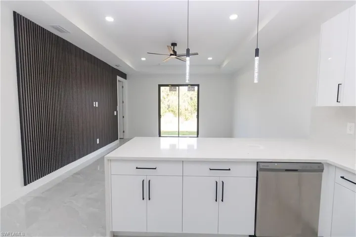 Kitchen featuring white cabinets, dishwasher, a peninsula, light stone countertops, and a ceiling fan