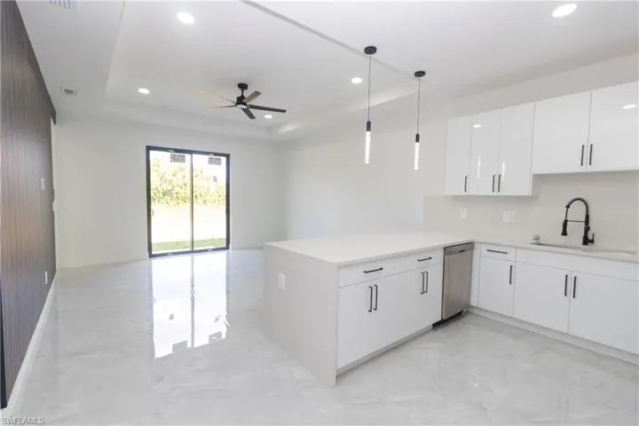 Kitchen featuring white cabinets, light stone counters, pendant lighting, light marble finish floors, and a tray ceiling