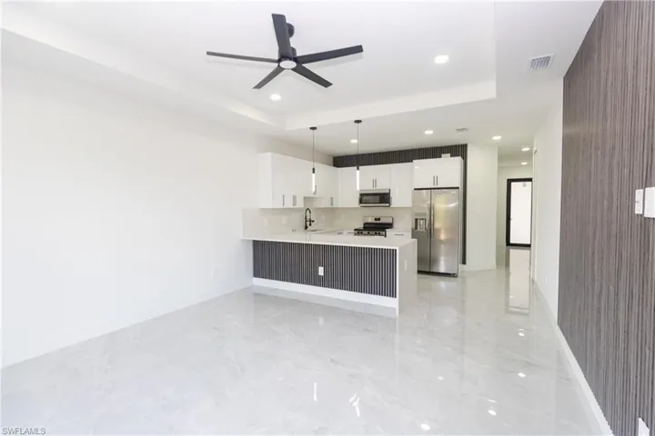 Kitchen with a peninsula, stainless steel appliances, white cabinetry, decorative light fixtures, and ceiling fan