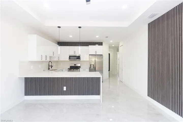 Kitchen with pendant lighting, white cabinets, stainless steel appliances, a peninsula, and light stone counters