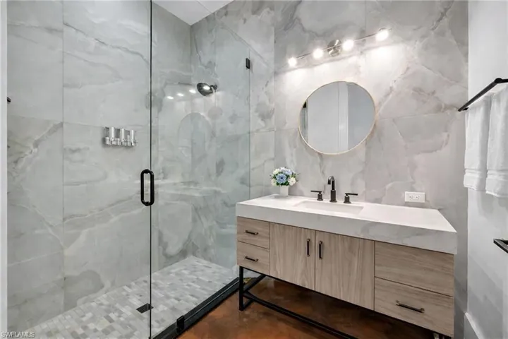 Bathroom featuring vanity, a marble finish shower, and tile walls