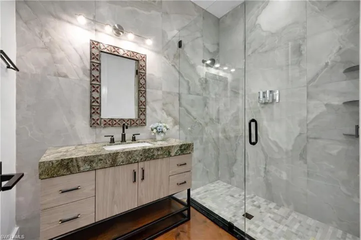 Bathroom with vanity, a marble finish shower, and tile walls