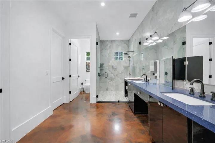 Bathroom featuring double vanity, a marble finish shower, recessed lighting, and finished concrete flooring