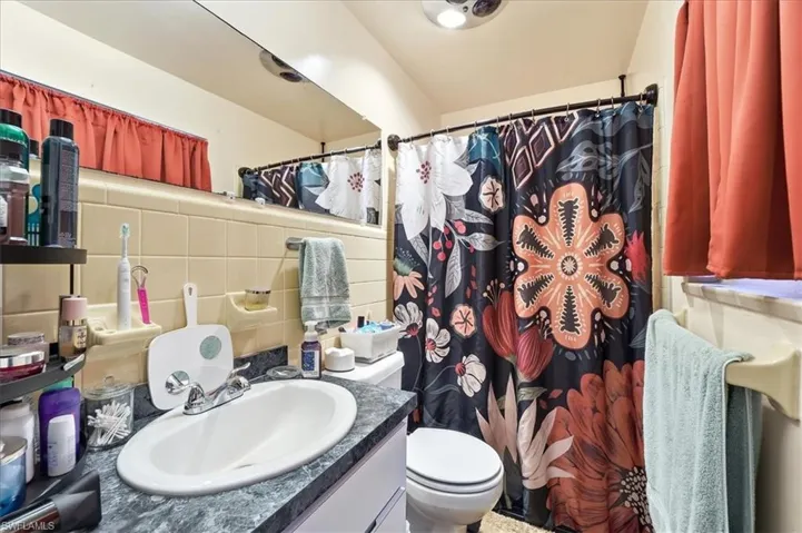 Full bath featuring a shower with shower curtain, vanity, tile walls, and tasteful backsplash