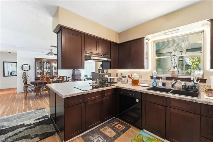Kitchen with dark wood finish cabinetry, black appliances, ceiling fan, and light wood-style floors