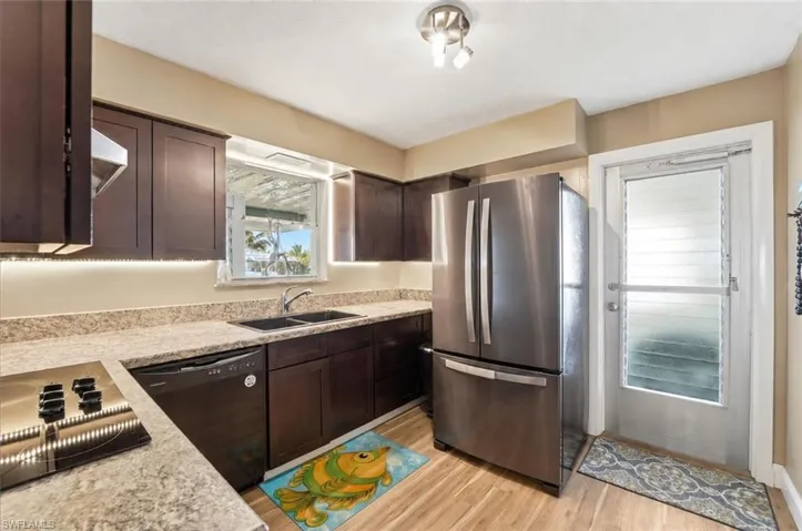 Kitchen featuring wood-finish flooring, dark wood cabinetry with under-cabinet lighting, light-toned countertops, and a stainless steel French door refrigerator
