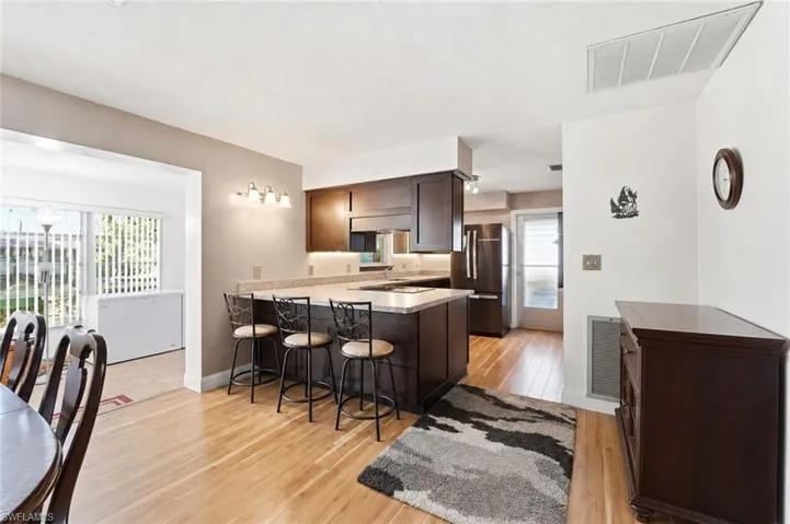 Kitchen featuring wood-finish flooring, dark wood cabinetry, stainless steel appliances, and a central island with bar seating