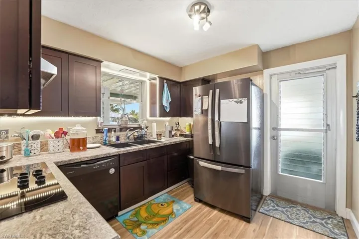 Kitchen with dark wood finish cabinetry, black appliances, light wood-type flooring, and light stone counters