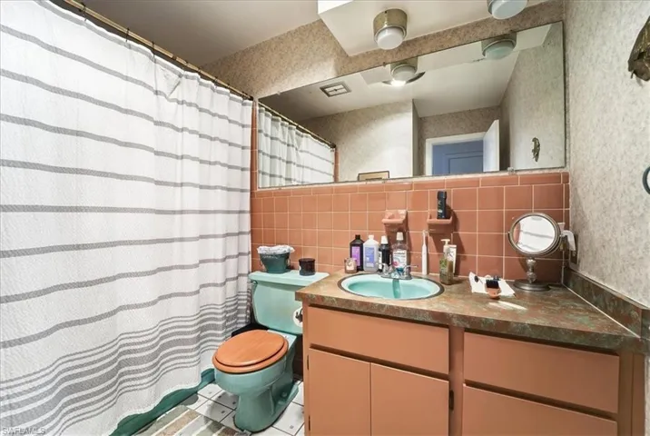 Full bath featuring a shower with shower curtain, vanity, wallpapered walls, tile walls, and tasteful backsplash