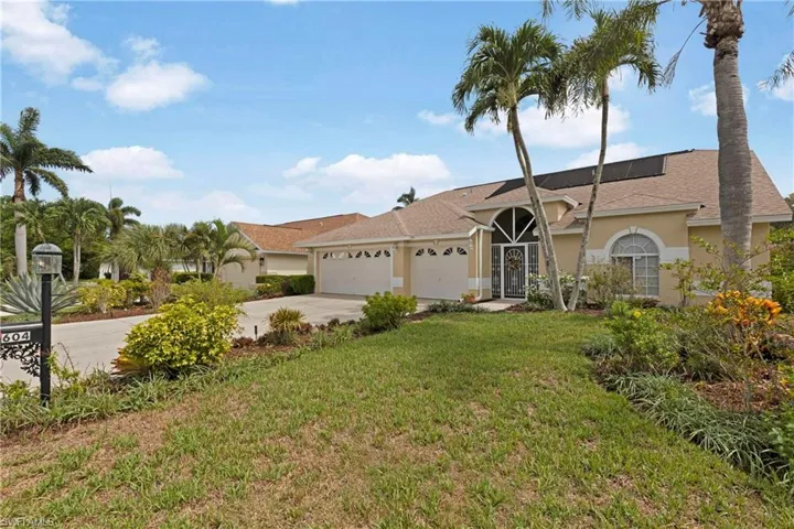 View of front of property with stucco siding, driveway, an attached garage, a front yard, and roof mounted solar panels