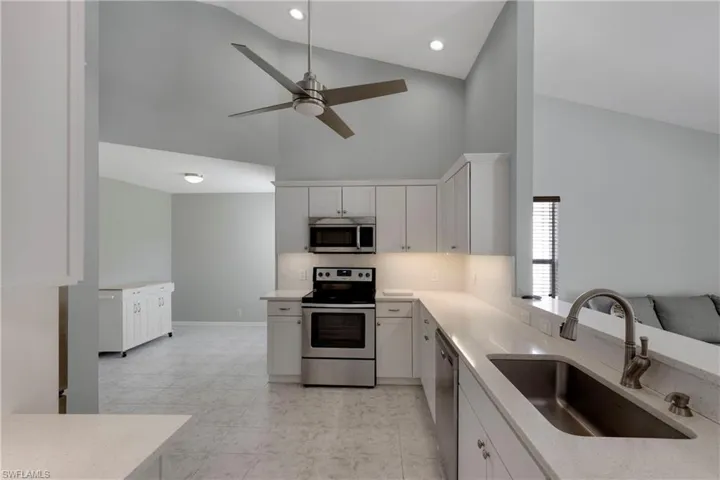 Kitchen featuring appliances with stainless steel finishes, a sink, high vaulted ceiling, a ceiling fan, and white cabinets