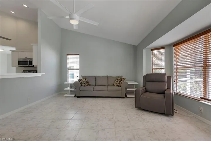 Living room with plenty of natural light, a ceiling fan, high vaulted ceiling, and baseboards