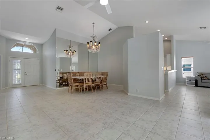 Dining space with high vaulted ceiling, a chandelier, light tile patterned floors, a ceiling fan, and baseboards