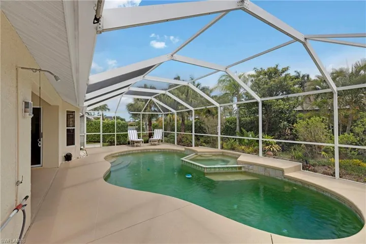 View of swimming pool with a patio area, glass enclosure, and a pool with connected hot tub.