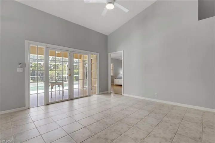 Empty room featuring high vaulted ceiling, french doors, tile patterned floors, ceiling fan, and baseboards