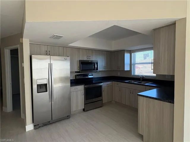 Kitchen featuring stainless steel appliances, dark countertops, and light brown cabinets