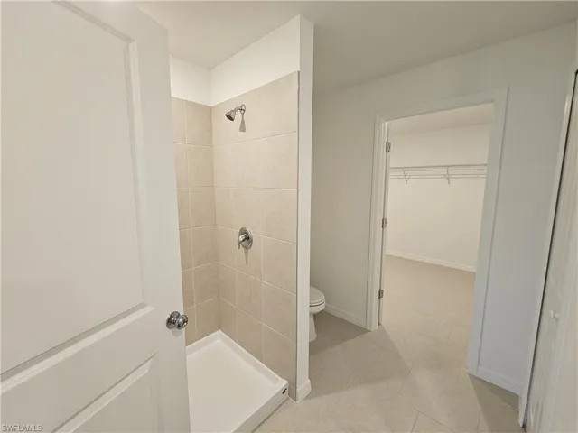 Walk-in shower featuring light-toned tile surround and chrome fixtures