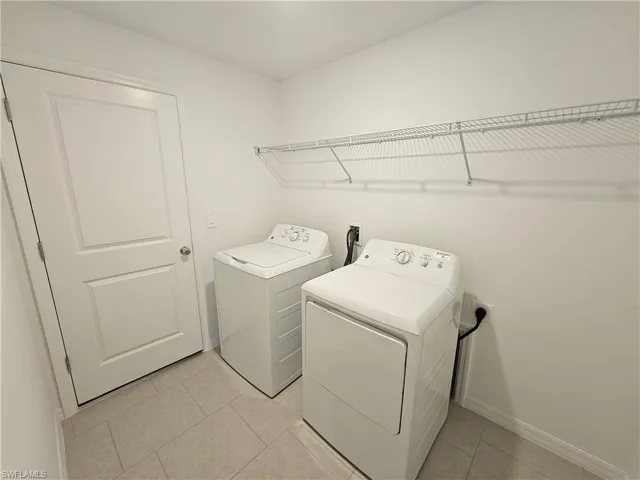 Dedicated laundry space featuring neutral-toned tile flooring, white walls, and a wire shelving unit