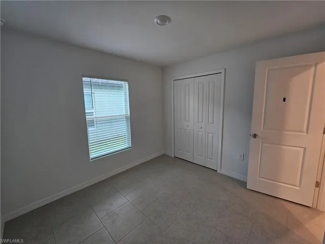 Room featuring square tile flooring, white baseboards, and a window with horizontal blinds
