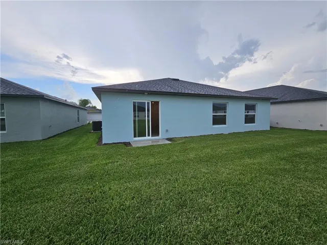 Rear exterior featuring light blue stucco siding, a dark shingle roof, and a sliding glass door