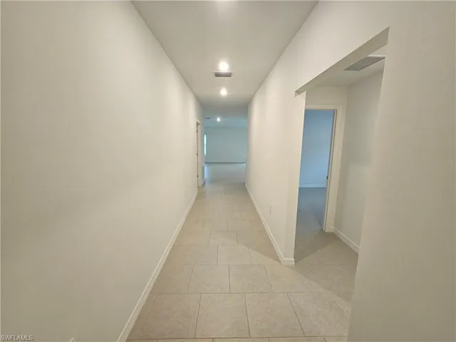 Hallway featuring light-toned tile flooring, recessed lighting, white baseboards, and doorways leading to additional rooms