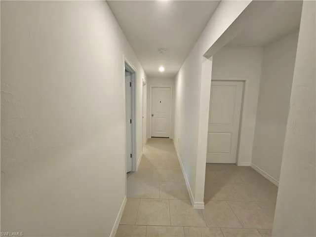 Hallway featuring light-toned tile flooring, recessed ceiling lighting, crisp white walls, and paneled interior doors